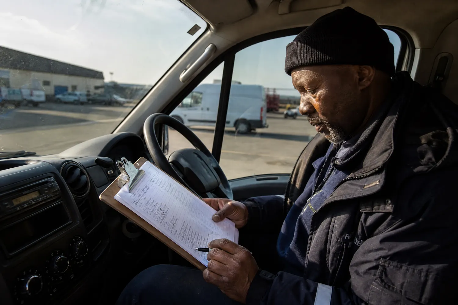 A driver reviews a cost worksheet on a clipboard in the cab of his van.