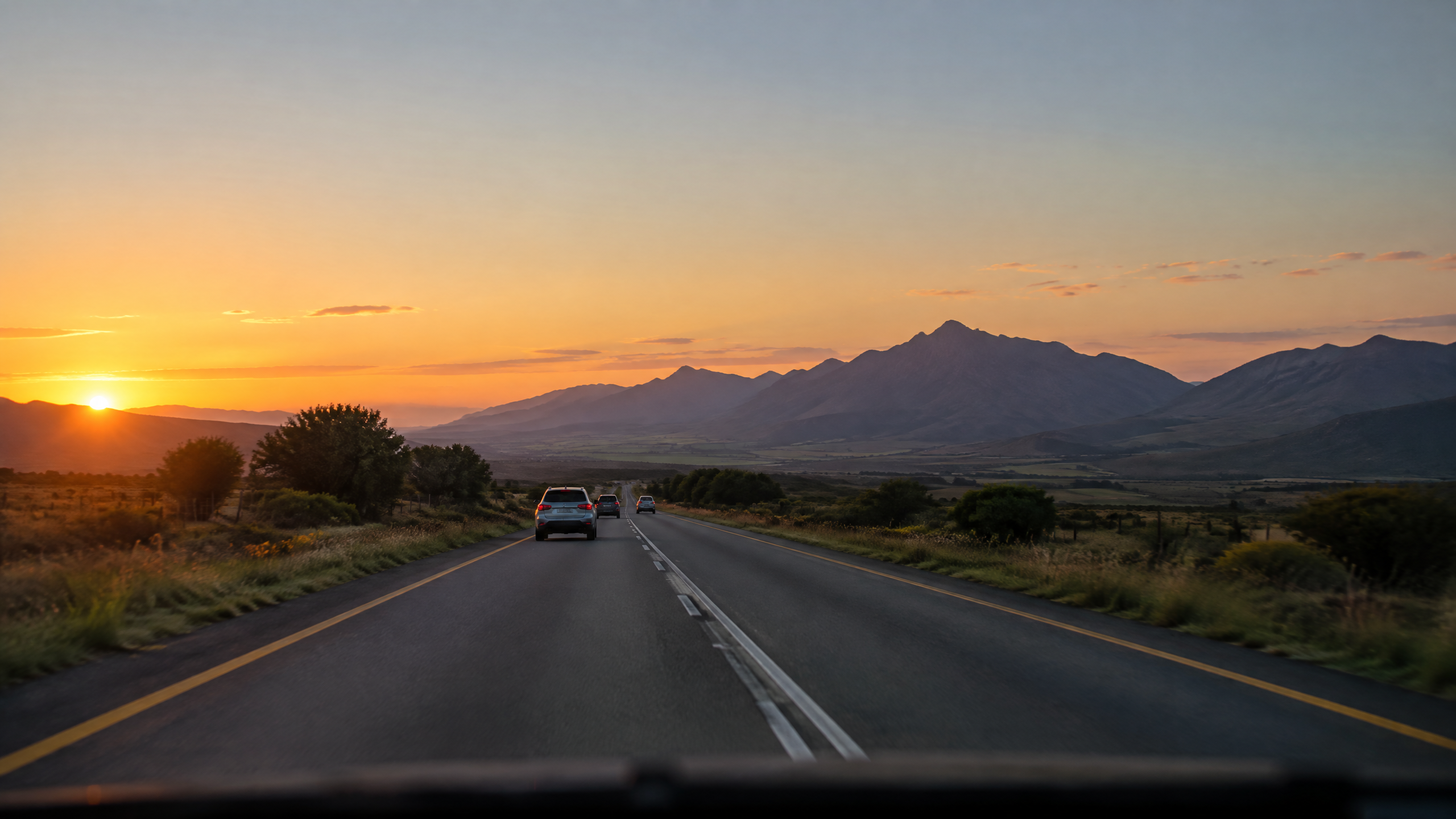A driver scanning the road ahead through a windshield, hands at ten and two on the steering wheel.