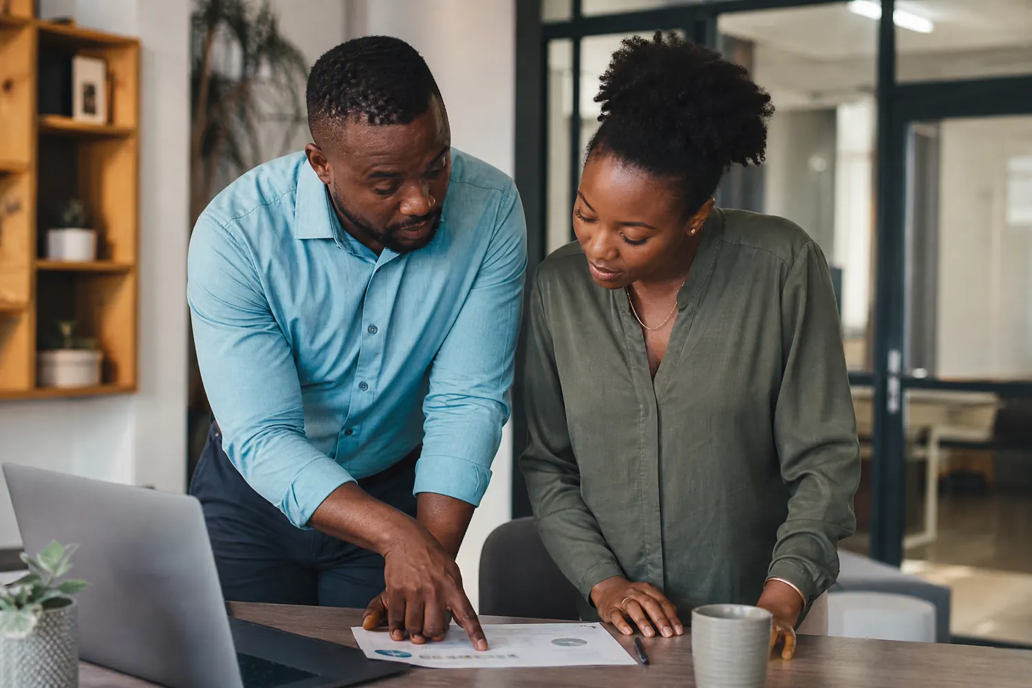 A manager coaches a colleague one-on-one at a desk, pointing out a detail on a document.