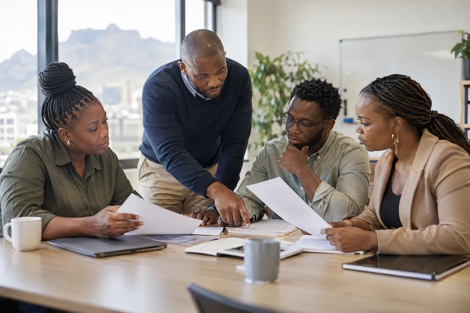 A supervisor points out a section of a printed policy document to three employees around a meeting table.